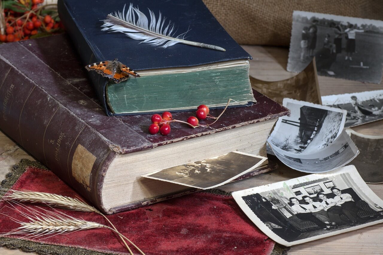 Livres anciens et photos anciennes en noir et blanc dans un décor avec un papillon, une plume et des fruits rouges