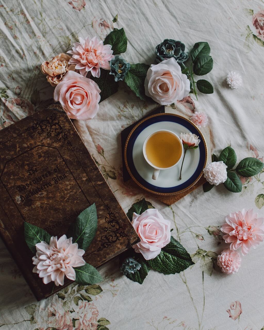 Tasse de thé posée auprès d'un livre ancien avec des fleurs roses disposées autour