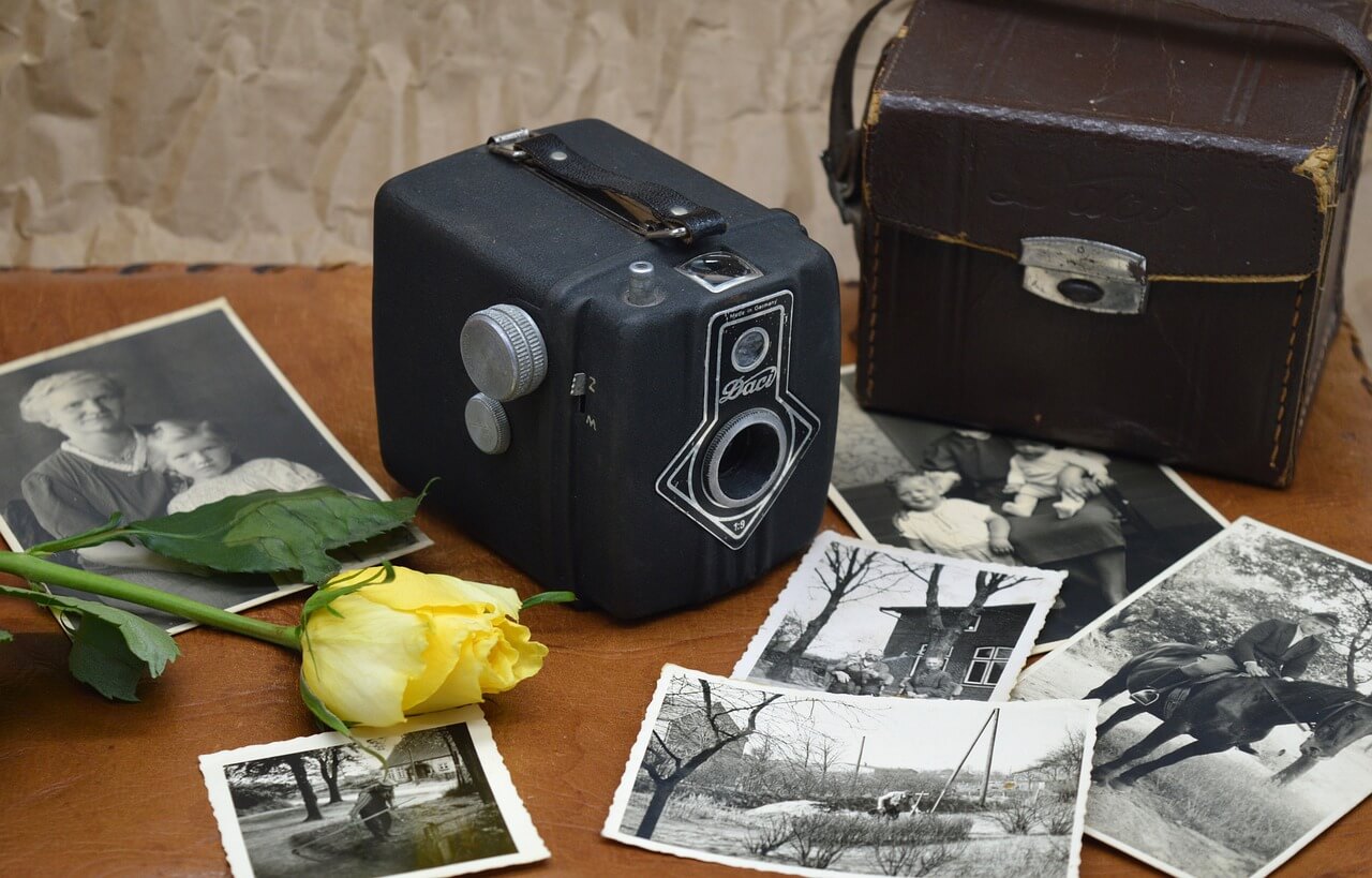 Vieille camera posé preès de photos anciennes en noir et blanc ainsi qu'une rose jaune